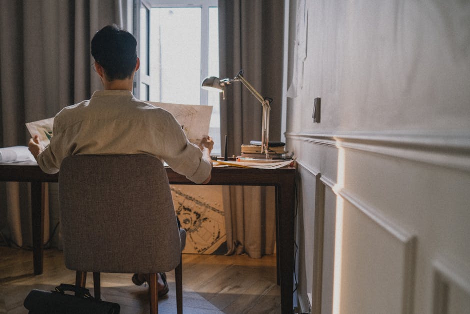 Caucasian man with black hair reviewing architectural plans in a home office setting.